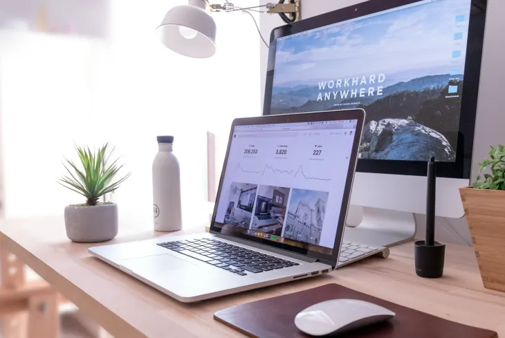 Schreibtisch mit Laptop und Monitor, auf denen eine Website geöffnet ist
